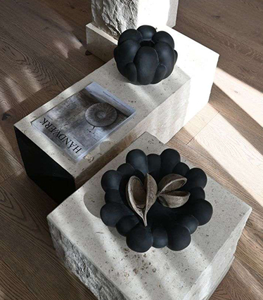 Artistic black ceramic bowls displayed on minimalist stone tables with natural textures