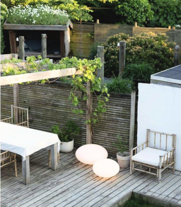 Stylish wooden terrace with white outdoor furniture and two softly glowing, round floor lamps in a tranquil garden atmosphere.