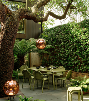 Tom Dixon outdoor lamps in a stylish garden with dining area under an old tree.