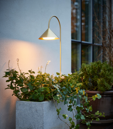 Luminous outdoor lamp by Frandsen next to a planted concrete tub on a terrace in front of a modern house façade.