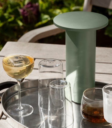 Sage green cylindrical side table/cooler on a tray with glasses and drinks outdoors.